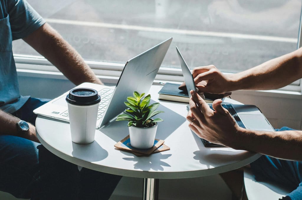 Two professionals working on laptops and tablet at a small table discussing a project