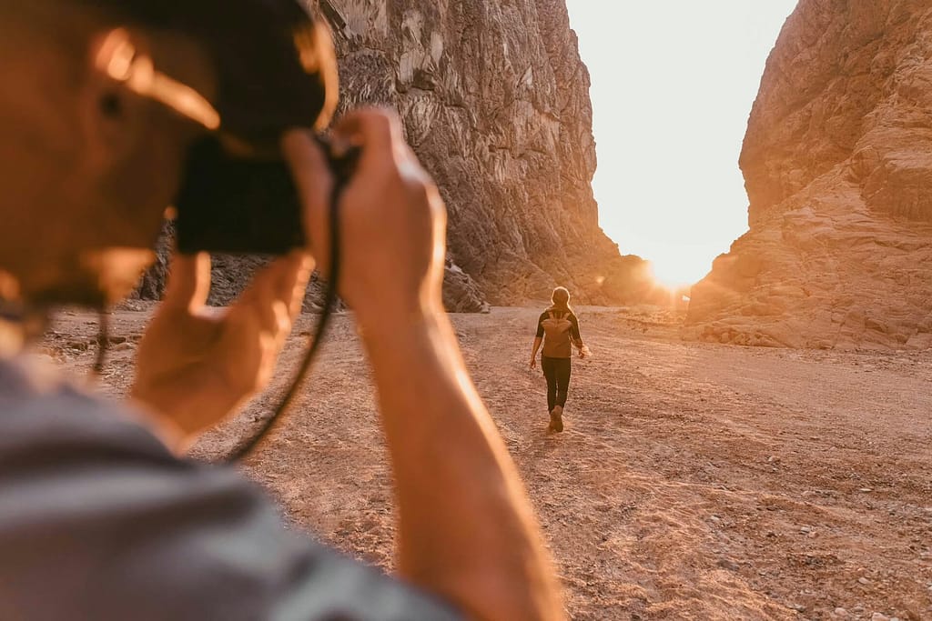 Traveler walking through a canyon at sunset while being photographed